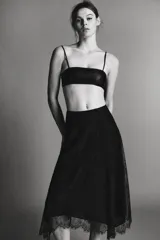 Falda midi negra de tiro medio, confeccionada en tejido de encaje con forro interior a tono. Presenta un bajo asimétrico con terminación en línea evasé y cierre lateral oculto.