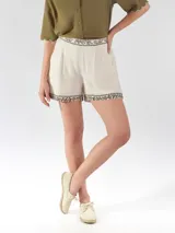 Short de lino color beige con detalles bordados en tono oscuro en la cintura y en el ruedo. Cuenta con cintura elástica fruncida y bolsillos laterales.