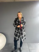 Abrigo de corte trench con estampado de tartán en tonos negro y gris. Presenta solapas amplias, bolsillos frontales y diseño abierto.