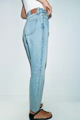 Jeans de denim azul claro lavado, tiro alto, corte Mom Fit con pierna recta y largo tobillero. Presenta cinco bolsillos y cierre frontal con cremallera y botón.