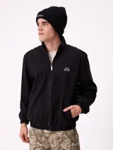 Gorro tipo beanie de punto acanalado en color beige, con parche rectangular negro con el logo de la marca en el frente.