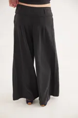 Pantalón de jean con diseño de tiro medio-bajo y piernas anchas. Presenta una pretina ancha con cierre de tres botones metálicos frontales, pinzas decorativas en la cintura y bolsillos delanteros funcionales.