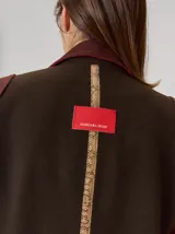 Tapado de lana color marrón oscuro, con corte a la rodilla, cintura ligeramente entallada y cierre frontal con botones. Presenta detalles en tono contrastante en los hombros y laterales.