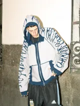 Hoodie con cierre frontal, tejido en algodón con diseño reversible. Presenta detalles de roturas intencionales en puños, ruedo y costuras, con estampado gráfico en mangas y capucha.
