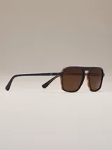 Lentes de sol con montura azul y lentes marrones. Diseño cuadrado con doble puente y patillas marrones con detalles a rayas.