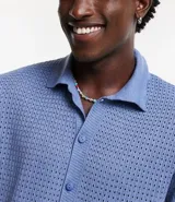 Camisa celeste de punto calado con cuello inglés, manga corta y abotonadura frontal.