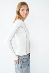 Sweater de manga larga color crudo, confeccionado en tejido de canalé elasticado. Diseño ajustado con cuello redondo y costuras decorativas en contraste color rosado en el frente, la espalda y las mangas.