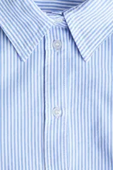 Camisa de corte relajado con diseño a rayas finas en tonos celeste y blanco, cuello clásico, mangas largas con puños anchos abotonados y bajo redondeado.