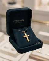 Dije en forma de cruz de acero inoxidable con acabado dorado y textura en los extremos.