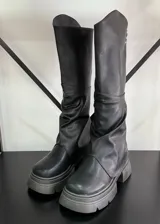 Botas negras de cuero vegano con caña alta, polainas arrugadas y suela track.