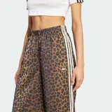 Pantalón Adidas Originals de pierna ancha, confeccionado en satén con estampado animal print de leopardo. Cuenta con cintura elástica, las clásicas tres tiras blancas en los laterales y el logo del trifolio bordado en el frente.