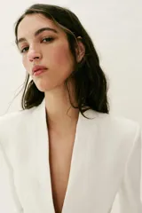 Blazer entallado color blanco de cuello sin solapa, manga larga con hombreras, falsos bolsillos delanteros de vivo y cierre frontal con un botón.