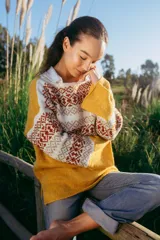 Sweater de lana merino color mostaza con diseño geométrico en blanco y marrón en la parte superior, mangas semi oxford y corte holgado.