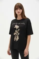 Remera negra de algodón con cuello redondo, mangas cortas y corte holgado. Presenta una estampa frontal en tono dorado con diseño floral y la inscripción "Poetry of nature".