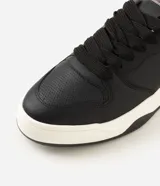Championes urbanos estilo skate de color negro con suela bicolor blanca y negra, talón gris y detalles perforados en la puntera.