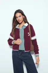 Campera de punto tipo cardigan en color bordó, con cierre frontal, cuello redondo y diseño estilo universitario. Presenta el número 54 bordado en blanco en el pecho y franjas blancas en las mangas.