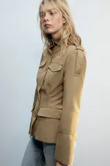 Cazadora de estilo militar en color tostado, con cuello subido, cierre frontal con botones y múltiples bolsillos con solapa en el pecho y la cintura. Cuenta con mangas largas con trabillas en los hombros.