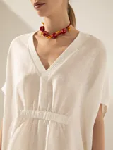Túnica blanca de lino con corte asimétrico, mangas cortas y escote en V con pespuntes.