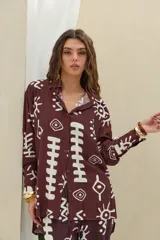 Camisa de manga larga color marrón oscuro con estampado gráfico en color blanco de símbolos abstractos, ojos y soles. Posee cuello camisero y cierre frontal con botones.