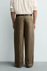 Pantalón de corte relajado confeccionado en mezcla de algodón y lino, con diseño de pliegues frontales, bolsillos laterales y bolsillos traseros de vivo. Presenta cierre frontal con cremallera y botón, con un acabado de lavado especial que le otorga una apariencia única.