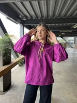 Canguro con capucha y cordones ajustables, confeccionado en tejido de punto. Presenta mangas largas abullonadas con puños elásticos y un parche de cuero sintético con logo en el pecho.