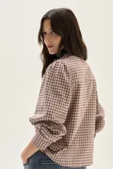 Camisa de manga larga con diseño de cuadros en tonos rosa y bordó. Presenta cuello mao, cierre frontal con botones y detalles de bordados florales en la parte superior del pecho. Las mangas son abullonadas con puños ajustados.