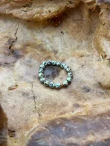 Anillo elástico de cuentas redondas de piedra dálmata con una cuenta dorada.