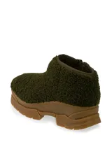 Zapatilla baja color verde oscuro con textura de piel de oveja y suela marrón con plataforma.