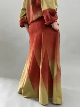 Falda larga de lana con diseño de paneles geométricos y efecto degradado que transiciona de verde esmeralda a tonos amarillentos. Presenta cintura alta, cierre invisible lateral y bolsillos ocultos.