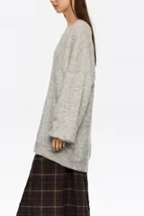 Jersey de punto largo con corte oversize, escote en pico pronunciado y mangas largas con volumen. Incluye un top interior de tirantes en satén con detalles de encaje en el escote.