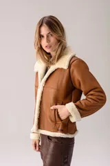 Campera tipo gamulán de cuero color tostado con interior y detalles en piel sintética color crema. Presenta cuello solapa, cierre frontal y mangas largas con puños de piel.