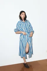 Trench largo de Zara con estampado de cuadros vichy en azul y blanco. Presenta cuello solapa, cierre frontal con botones, mangas largas y cinturón ajustable del mismo tejido. Incluye bolsillos de vivo en la parte delantera.