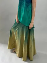 Falda larga de lana con diseño de paneles geométricos y efecto degradado que transiciona de verde esmeralda a tonos amarillentos. Presenta cintura alta, cierre invisible lateral y bolsillos ocultos.