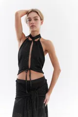 Top halter de tejido con lúrex en color negro, con abertura frontal y cordones ajustables para atar.