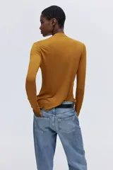 Top de punto mostaza con cuello alto y mangas largas, con detalles de terminación ondulada en puños y bajo.