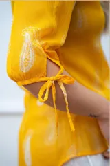 Blusa amarilla de gasa estampada con arabescos blancos, de corte irregular y mangas tres cuartos con lazo.