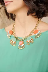 Collar de cadena gruesa dorada con dijes de piedras en tonos naranja y verde claro, decorados con pequeños cristales y colgantes metálicos en forma de flecos.
