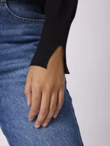 Buzo de punto fino color marrón topo, con cuello redondo y detalle de botones decorativos dorados sobre el hombro izquierdo. Presenta mangas largas con puños acanalados y una pequeña abertura lateral en los mismos.