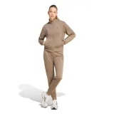 Conjunto deportivo Adidas Essentials Feel Cozy para mujer, compuesto por campera de cierre frontal con cuello alto y bolsillos laterales, y pantalón tipo jogger a juego. Presenta diseño liso en color marrón con el logo de la marca bordado discretamente en el pecho y en la pierna.