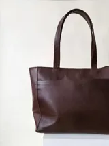 Cartera tipo shopper de cuero marrón texturado, con doble asa de hombro y un bolsillo frontal amplio con cierre de imán.