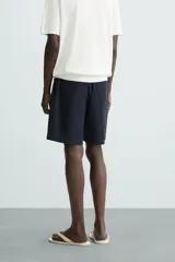 Bermuda azul marino de corte regular fit, confeccionada en tejido de algodón y lino. Cuenta con bolsillos frontales y traseros, cierre frontal con cremallera y botón.