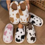 Pantuflas sin talón confeccionadas en algodón afelpado y piel sintética, con divertido estampado de manchas de vaca en tonos blanco y marrón, y suela de PVC.