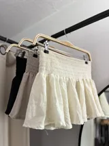 Minifalda de tiro bajo color beige, con cintura elástica fruncida y diseño acampanado con volados.