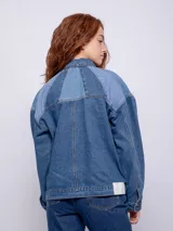 Campera de jean azul con recortes en diferentes tonos de denim, corte oversize, cuello camisero, cierre frontal con botones metálicos y bolsillos delanteros.