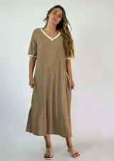 Vestido midi dorado con brillo, escote en V con ribete blanco y mangas cortas con puños blancos. Tiene aberturas laterales en el ruedo.