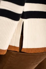 Sweater de punto con diseño a rayas horizontales en color negro y crema, de corte oversize. Presenta cuello redondo, mangas largas con puños acanalados y un detalle de borde inferior en color cobre con acabado brillante.
