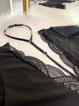 Body entallado de lycra color negro, con escote pronunciado decorado con encaje y microtul. Presenta mangas cortas de encaje y un collarín regulable desmontable integrado al diseño.