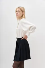 Falda corta negra plisada, de tiro alto con pretina ancha.