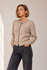 Cardigan de punto color beige con ribetes oscuros, cuello redondo, cierre frontal con botones y detalle de bordado en el pecho.