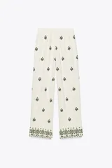 Pantalón color crema de tiro medio con cintura elástica ajustable y bolsillos delanteros. Presenta bordados florales en negro y corte ancho.